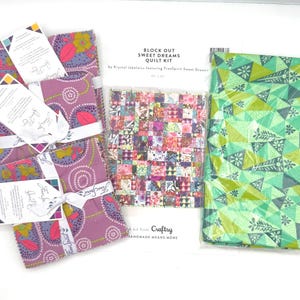 May include: A quilt kit with various fabric bundles in shades of purple, pink, and green. The kit includes a package of pre-cut fabric squares and a larger piece of patterned fabric. The text on the packaging reads "Block Out Sweet Dreams Quilt Kit."