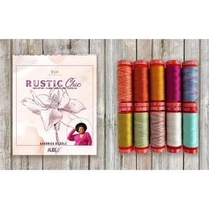 May include: A set of ten spools of Aurifil 100% cotton thread in various colors, accompanied by a rectangular box featuring a floral illustration, the text RUSTIC Chic, and a photograph of a person wearing a pink top and black hat.