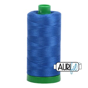 May include: A spool of vibrant blue sewing thread featuring a green plastic top and base. The brand name AURIfil is printed in black and blue text on a white rectangular label attached to the lower right side of the blue thread spool.
