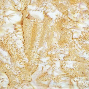 Puede incluir: Una pieza de tela con un patr&oacute;n batik sobre una base blanca, con formas org&aacute;nicas texturizadas y moteadas en amarillo dorado y marr&oacute;n claro. El dise&ntilde;o muestra un efecto craquelado de reserva de cera con intensidad de color variable.