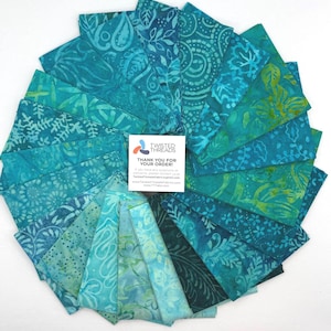 May include: A collection of teal and blue fabric squares arranged in a circular fan pattern, featuring various batik-style floral and geometric prints. A white square card in the center displays the text Twisted Threads Thank You For Your Order.