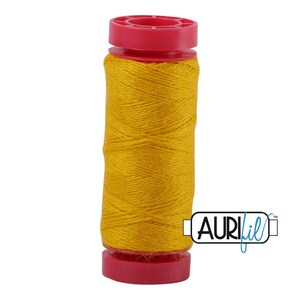 May include: A spool of vibrant golden yellow thread wound around a cylindrical core with bright pink plastic caps at the top and bottom. The brand name AuriFil is printed in black and blue text on a white rectangular label attached to the side.