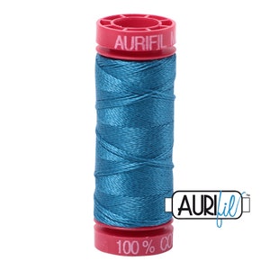 May include: A spool of teal blue Aurifil thread with a red label that says "Aurifil 100% Cotton" and a white label that says "Aurifil".