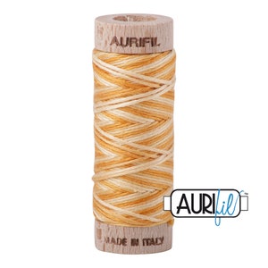 May include: A spool of Aurifil thread in a light orange and cream color combination. The spool is made of wood and has the Aurifil logo printed on it. The text "Made in Italy" is printed on the bottom of the spool.