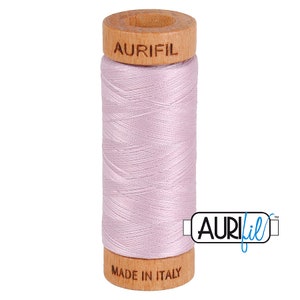 May include: A spool of pale pink thread with a wooden bobbin. The bobbin is labeled "Aurifil" and "Made in Italy".