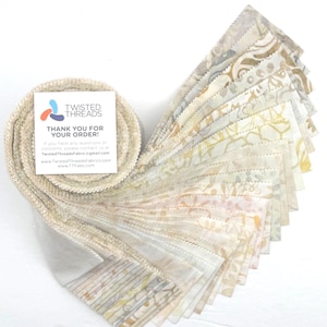 May include: A jelly roll of fabric strips featuring a variety of cream, beige, and soft yellow floral and geometric patterns. A square white card is attached to the roll with the text Twisted Threads Thank You For Your Order and contact info.