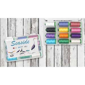 May include: A clear plastic storage box with a white label that says "SeaSide" and features a variety of birds and a heron. The box contains 12 spools of colorful embroidery floss.