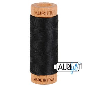 May include: A spool of black sewing thread wound around a light-colored wooden core. The top of the wooden spool is embossed with the text AURIFIL, and the bottom is embossed with the text MADE IN ITALY. A logo for Aurifil is visible on the right.