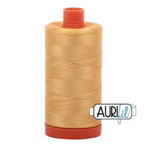 May include: A spool of golden-yellow sewing thread with a cylindrical shape. The thread is wound tightly around a central core, featuring a bright orange plastic cap at the top and an orange base. The logo AuriFil is printed on the lower right.