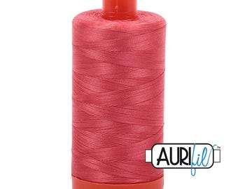 May include: A cylindrical spool of vibrant coral-pink sewing thread featuring a matching plastic top and base. The spool is wrapped with smooth, tightly wound thread and displays the brand name AuriFil in a black and blue logo on the side.