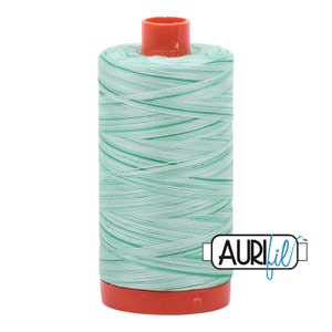 May include: A spool of light green and white thread with a red plastic bobbin. The thread is wound tightly and has a subtle sheen. The spool is labeled "Aurifil" in blue lettering.