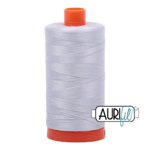 May include: A spool of light gray sewing thread featuring a bright orange plastic top and bottom cap. The spool is cylindrical with a smooth, tightly wound surface. The brand name AURIfil is printed in black and blue text on the lower right side.
