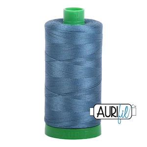 May include: A spool of blue sewing thread with a green plastic top and base. The spool features a label with the text AuriFil in black and blue lettering. The thread is wound tightly around the cylindrical core, displaying a smooth texture.