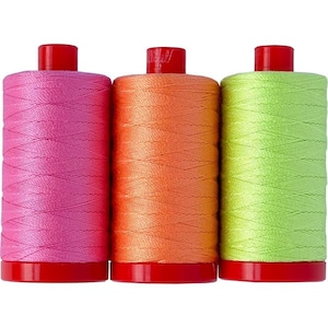 May include: Three cylindrical spools of sewing thread arranged side by side. The left spool is bright pink, the center spool is vibrant orange, and the right spool is lime green. Each spool features a solid red plastic cap and base.