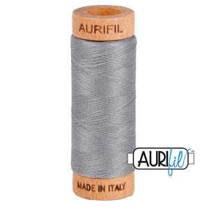 May include: A spool of grey sewing thread wound around a wooden core. The top of the wooden spool is branded with the text AURIFIL, and the bottom is branded with the text MADE IN ITALY. The thread is tightly coiled in a smooth, uniform pattern.