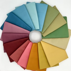 May include: A circular arrangement of folded fabric swatches in a variety of colors, including blues, greens, pinks, and yellows. The swatches are fanned out from a central white circle, showcasing a spectrum of hues. Ideal for quilting or crafting projects.