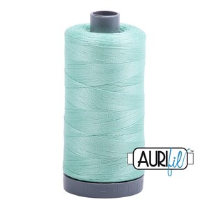 May include: A spool of light mint green sewing thread with a dark gray plastic core. The thread is wound tightly around the cylindrical spool. The AuriFil brand logo is printed in black and blue text on the lower right side of the image.
