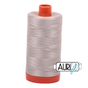 May include: A spool of light taupe sewing thread featuring a bright orange plastic top and base. The spool is wrapped with smooth, tightly wound thread and includes a white rectangular logo with the black and blue text AURIfil.