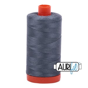 May include: A cylindrical spool of dark gray sewing thread featuring a bright orange plastic top and bottom cap. The spool is wrapped in smooth, tightly wound thread and displays the brand name AURIfil in a white rectangular logo with black text.