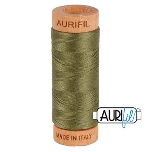 May include: A spool of olive green sewing thread wrapped around a light-colored wooden cylinder. The top of the wooden spool is branded with the text AURIFIL, and the bottom is branded with the text MADE IN ITALY. The thread is tightly wound.