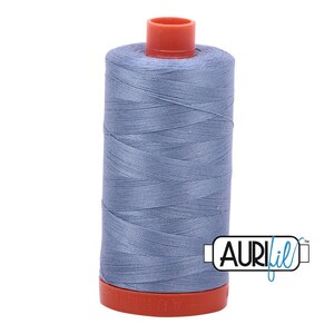 May include: A spool of light blue sewing thread featuring a cylindrical shape with a vibrant orange plastic base and top cap. The thread is wound tightly around the core, and the brand name Aurifil is printed in black text on the lower right side.
