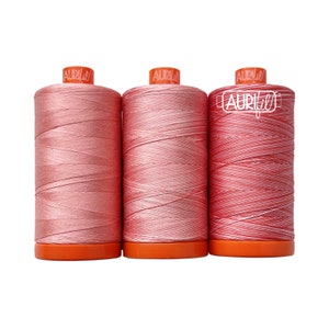 May include: Three spools of pink and white thread with orange bobbins. The thread is Aurifil brand.