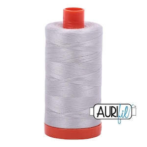 May include: A spool of light gray sewing thread wound onto a cylindrical plastic core with a bright orange top and bottom cap. The brand name AuriFil is printed in black and blue text on the lower right side of the spool against a white background.
