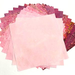 May include: A stack of square fabric swatches arranged in a fan shape. The collection features various shades of pink, ranging from pale pastel to deep magenta, with some pieces displaying intricate floral and abstract patterns with pinked edges.
