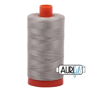 May include: A spool of light gray sewing thread wound around a cylindrical core with bright orange plastic caps at the top and bottom. The brand name AuriFil is printed in black and blue text on a white rectangular label on the lower right side.