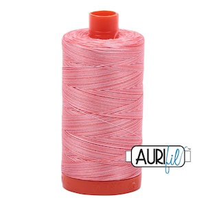May include: A spool of pink and white Aurifil thread with the Aurifil logo on the side.