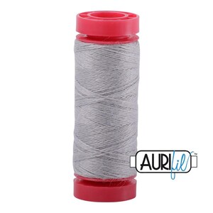 May include: A spool of light gray sewing thread wound around a cylindrical core with bright red plastic caps at the top and bottom. The brand name AuriFil is printed in black and blue text on a white rectangular label next to the spool.