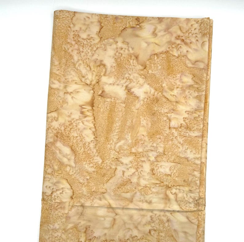 Puede incluir: Una pieza rectangular de tela con un patr&oacute;n moteado y jaspeado en tonos bronceado claro, beige y crema. La superficie muestra una textura org&aacute;nica e irregular con motas de color marr&oacute;n oscuro y parches m&aacute;s claros distribuidos.