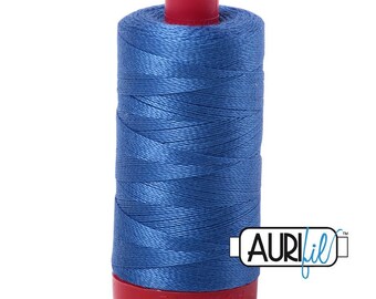 May include: A spool of blue sewing thread wound around a cylindrical core with a red plastic top and base. The brand name Aurifil is printed in black and blue text on a white rectangular label positioned to the right of the thread spool.