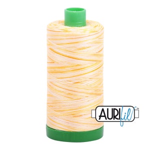 May include: A spool of Aurifil thread in a yellow and white variegated color. The spool is green and has the Aurifil logo on it.