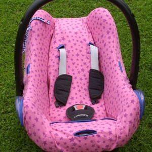 May include: Pink baby car seat cover with a star pattern and blue trim. The cover has a CabrioFix label.