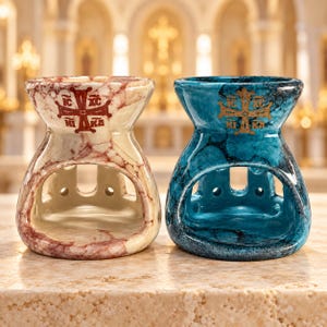 Op de afbeelding: Twee keramische oliebranders met een marmerachtige afwerking. De ene brander is crème met rode aders en een rood kruissymbool met de tekst IC XC NI KA. De andere brander is blauw met donkerblauwe aders en een gouden kruis met de tekst IC XC NI KA.