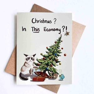 Peut inclure: Carte de Noël avec un chat grincheux et un sapin décoré. Le texte dit "Christmas? In This Economy?!" en noir. La carte est sur fond blanc, avec une enveloppe marron.