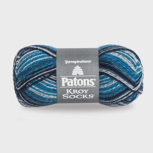 May include: A skein of Patons Kroy Socks yarn featuring a variegated color palette of navy blue, bright blue, and light grey stripes. A grey paper label is wrapped around the center with the text Yarnspirations, Patons, and KROY SOCKS.