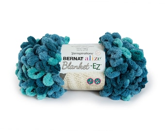 Puede incluir: Una madeja de hilo Bernat Alize Blanket-EZ con una paleta de colores variados en azul cerceta profundo, azul marino y turquesa brillante. El hilo tiene una textura de bucles preformados y una etiqueta de papel blanco con el texto 6.4 oz / 180 g.
