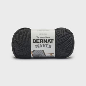 Könnte beinhalten: Dunkelgrauer Wollknäuel mit weißem Etikett, auf dem "BERNAT MAKER" und "8.8 oz / 250 g" stehen. Das Garn ist dick und wirkt weich, ideal für Strick- oder Häkelprojekte. Das Gewicht beträgt 250 Gramm.