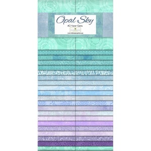 Pode incluir: Um pacote de 42 quadrados de tecido de 6,35 cm em um degradê de azul, roxo e verde com vários padrões. O pacote é rotulado como "Opal Sky 42 Karat Gems".