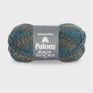 Peut inclure: Une pelote de laine aux tons variés de bleu sarcelle, de brun et de beige. Une étiquette en papier gris entoure le centre, avec le texte blanc Yarnspirations, Patons et KROY SOCKS FX, ainsi qu'une petite icône en forme de ruche.