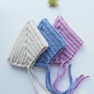 Peut inclure: Trois bonnets de bébé en tricot de couleur crème, bleu clair et rose avec des liens assortis.