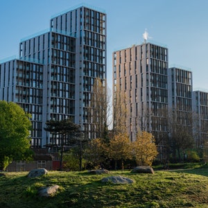 Peut inclure: Une rangée d'immeubles d'appartements modernes avec une zone herbeuse au premier plan. Les bâtiments sont en béton et en verre et ont un design élégant et contemporain.