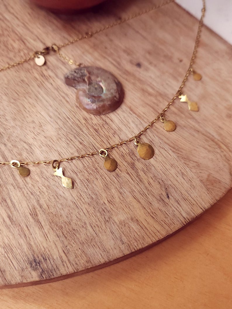 May include: A gold-toned chain necklace featuring small, dangling geometric charms in circular and diamond shapes. The necklace is accompanied by a separate, spiral-shaped fossil pendant with a brownish, textured surface and metallic highlights.
