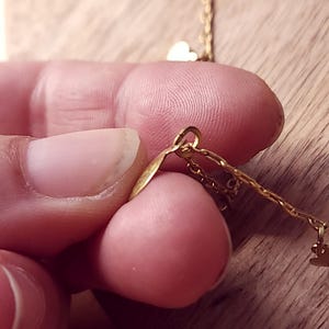 May include: A gold-toned metal chain necklace featuring small, delicate heart-shaped charms attached to the links. The chain is constructed with thin, interlocking oval links, and the heart charms are suspended at intervals along the length.