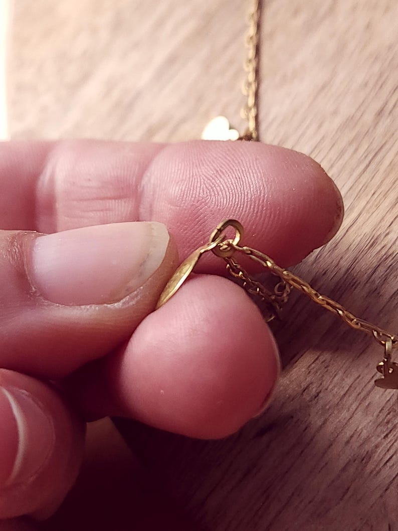 May include: A gold-toned metal chain necklace featuring small, delicate heart-shaped charms attached to the links. The chain is constructed with thin, interlocking oval links, and the heart charms are suspended at intervals along the length.