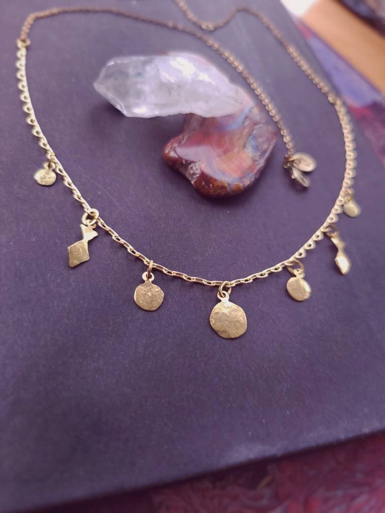 May include: A gold-toned chain necklace featuring a series of small, irregularly shaped, hammered metal charms dangling from the links. The necklace has a delicate, fine-link construction with a clasp closure and a small circular tag near the end.