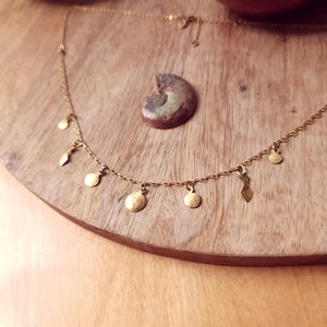 May include: A gold-toned chain necklace featuring a series of small, dangling charms in various shapes, including circular discs and elongated geometric forms, suspended at regular intervals along the delicate metal link chain.
