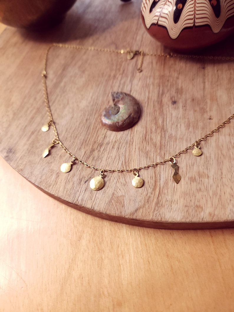May include: A gold-toned chain necklace featuring a series of small, dangling charms in various shapes, including circular discs and elongated geometric forms, suspended at regular intervals along the delicate metal link chain.